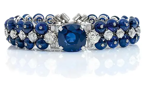 CARTIER EXCEPTIONEL BRACELET D'EPOQUE ART DECO La monture souple en platine et or gris retenant en son centre un important saphir de taille coussin facetté denviron 22 carats ( 14,4 x 14,5 x 11,4 mm ) épaulé de 2 diamants de taille brillant, taille ancienne denviron 1,50 carat dans un entourage de 4 diamants de taille baguette en console. La monture retenant une succession de 19 diamants de taille brillant en chute, épaulée dune double ligne sertie de 39 boules de saphirs et 1 pierre bleue sertis en leur dun diamant de taille brillant serti clos (environ 78 carats) Le fermoir à rabat serti d'une double ligne de 5 diamants de taille brillant et de 8 diamants de taille baguette formant un décor de chevrons. Poids brut : 67,46 g Longueur : 18 cm Dans un écrin de la maison Cartier.