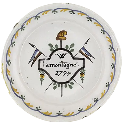 Description: Assiette creuse, à marli relevé et à bord rond. Décor polychrome en plein. Marques, inscriptions, poinçons: Inscription - Dans un cartouche au centre : "W / la montagne / 1794". Description iconographique: Cartouche agrémenté de feuillages et de chûtes de fleurs portant l'inscription "W. la Montagne, 1794" et masquant une pique coiffée du bonnet et de deux drapeaux tricolores.