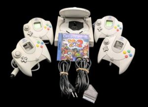 Sega - Console de salon - Dreamcast (Avec 1 jeu et accessoires dont 2 cartes mémoires VMU). Test d'allumage effectué avec succès - Jeu associé : Power Stone 2, avec son GD-ROM et sa notice. (Version du jeu PAL). Avec 4 manettes fonctionnelles, cordon d'alimentation, prise péritel, 2 cartes mémoires VMU. Version du jeu PAL.