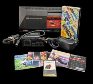 Sega - Console de salon - Master System. Test d'allumage non concluant. Avec cordon d'alimentation, câble péritel, un controller, une cassette SEGA, une cartouche de jeu HangOn, 3 notices de jeux.